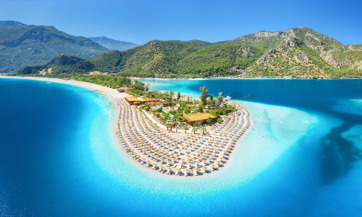 Fethiye-Aerial-view-of-sea-bay-sandy-beach-with-umbrellas-trees-mountain-at-sunny-day-in-summer.jpg